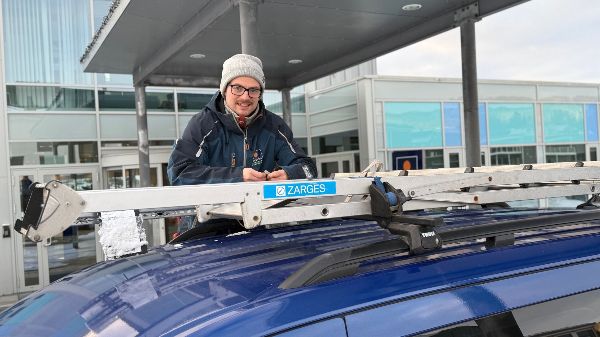 Bilde av en elektriker som fester en stige til taket på arbeidsbilen. Han ser i kameraet og smiler. 